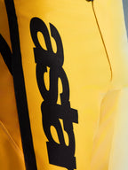 Närbild på Alpinestars 2026 Fluid Apex byxor, motocrossbyxor, gula och svarta, med en stor vertikal svart logotyp, texturerat slitstarkt material och ergonomiska detaljer för terrängprestanda
