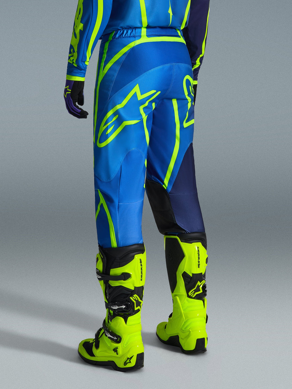 Alpinestars 2026 Fluid Apex Pants, Motocross Pants, Blue and Yellow Fluo, back view of rider wearing matching gear and fluorescent yellow boots, featuring bold Alpinestars logos and ergonomic design