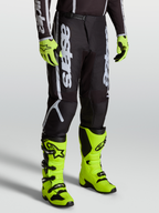 Alpinestars Fluid Apex V2 byxor, svarta och silver motocrossbyxor för herr, 600D polytyg, visas på modell med neongula stövlar