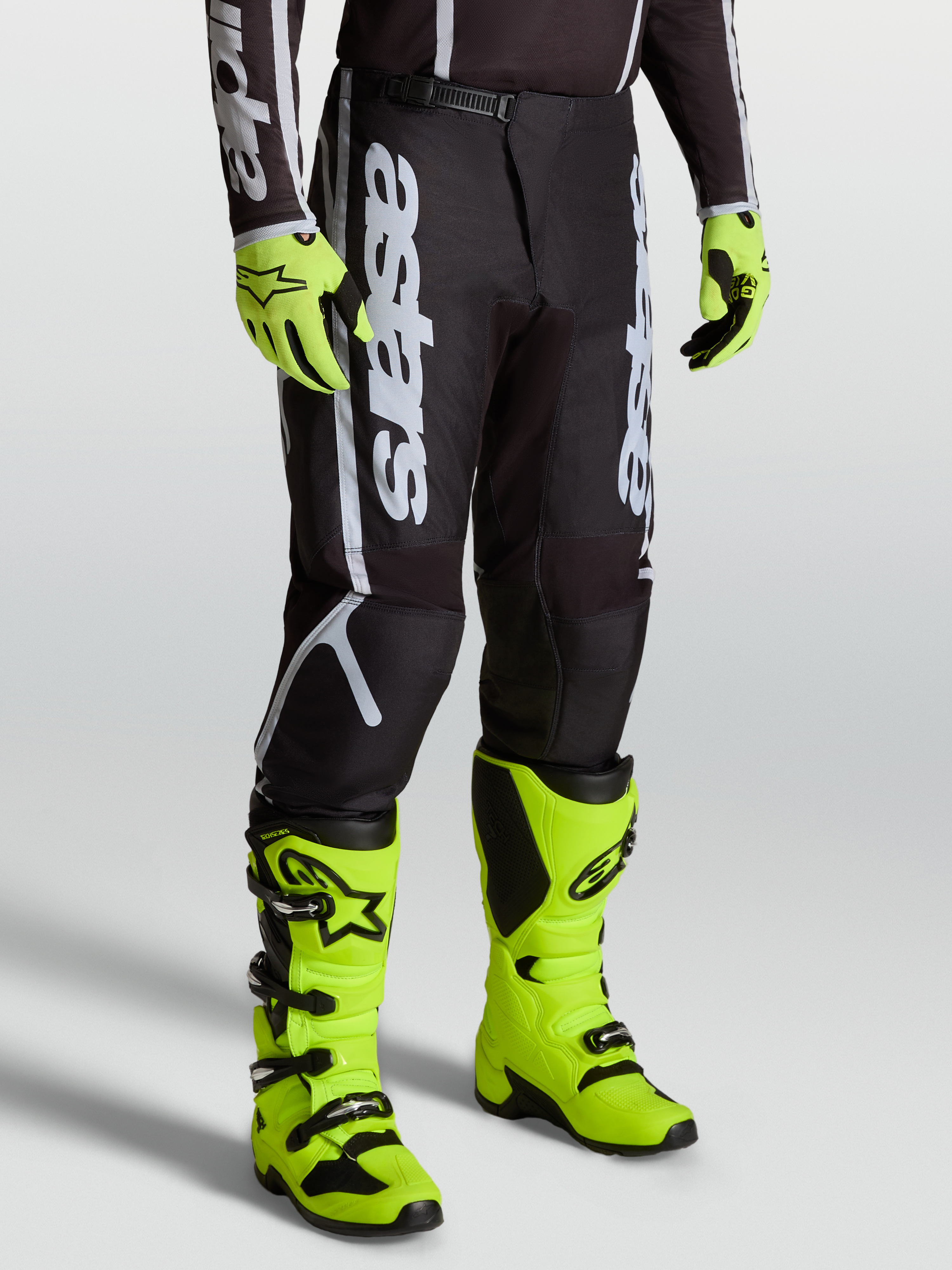Alpinestars Fluid Apex V2 byxor, svarta och silver motocrossbyxor för herr, 600D polytyg, visas på modell med neongula stövlar