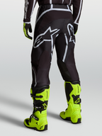 Alpinestars Fluid Apex V2 byxor, motocrossbyxor för herr i svart och silver, sedda bakifrån med neongula stövlar.