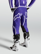 Alpinestars Fluid Apex V2 byxor, mörkblå och vita motocrossbyxor för herr, sedda bakifrån på modell med vita stövlar, stor stjärnlogotyp och ergonomisk 3D-skärning.