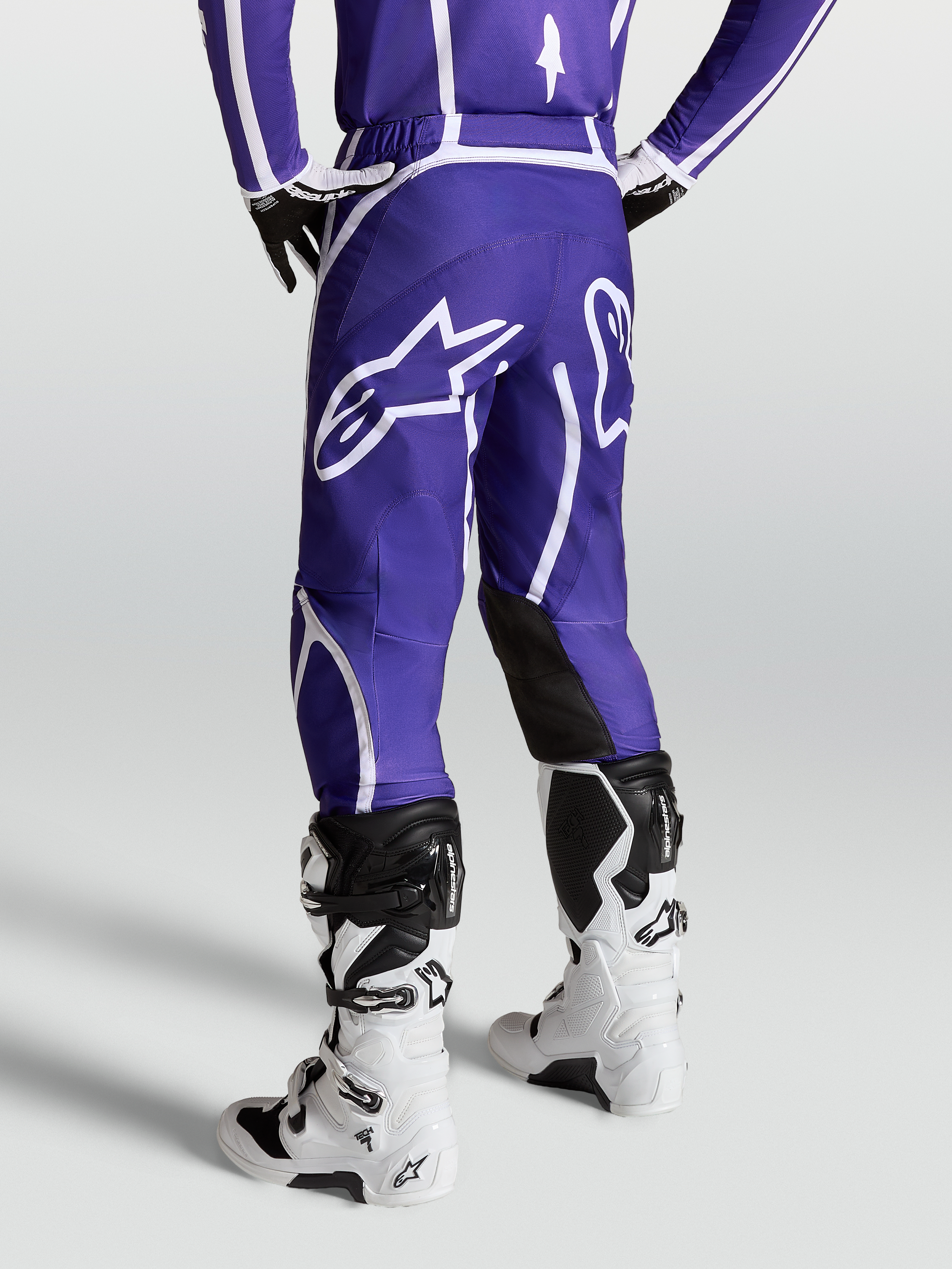 Alpinestars Fluid Apex V2 byxor, mörkblå och vita motocrossbyxor för herr, sedda bakifrån på modell med vita stövlar, stor stjärnlogotyp och ergonomisk 3D-skärning.