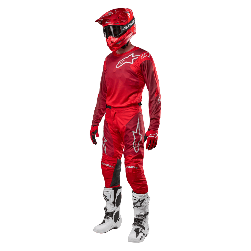 Motocrossförare i komplett racingutrustning, Alpinestars 2024 Racer Hoen byxor och tröja i Mars Red Burgundy, röd hjälm, röda handskar och vita och svarta stövlar, matchande outfit för terrängkörning