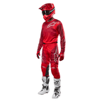 Motocrossförare i komplett racingutrustning, Alpinestars 2024 Racer Hoen byxor och tröja i Mars Red Burgundy, röd hjälm, röda handskar och vita och svarta stövlar, matchande outfit för terrängkörning