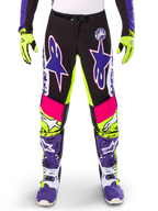 Alpinestars Limited Edition Supertech Dirt Studios byxor, motocrossbyxor, vit, lila och neongul, med svarta paneler samt neongula och rosa detaljer, stora lila stjärnlogotyper, visas med matchande neongula handskar och lila racingstövlar, hållbara kläder för terrängkörning