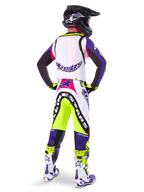 Motocrossförare i Alpinestars Limited Edition Supertech Dirt Studios® byxor i färgerna White Purple och Yellow Fluo, sedd bakifrån med matchande tröja, stövlar och svart kolfiberhjälm, professionell offroad-racingutrustning med kraftfull grafik och neonaccenter.