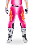 Alpinestars Limited Edition Supertech AFD MIG-byxor, motocross-racingbyxor, fluorescerande rosa och vita med orange detaljer, stora stjärnlogotyper på låren, perforerade paneler och svarta greppzoner vid knäna, bärs med vita och svarta motocross-stövlar
