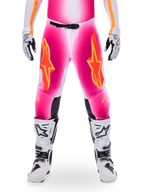 Alpinestars Limited Edition Supertech AFD MIG-byxor, motocross-racingbyxor, fluorescerande rosa och vita med orange detaljer, stora stjärnlogotyper på låren, perforerade paneler och svarta greppzoner vid knäna, bärs med vita och svarta motocross-stövlar