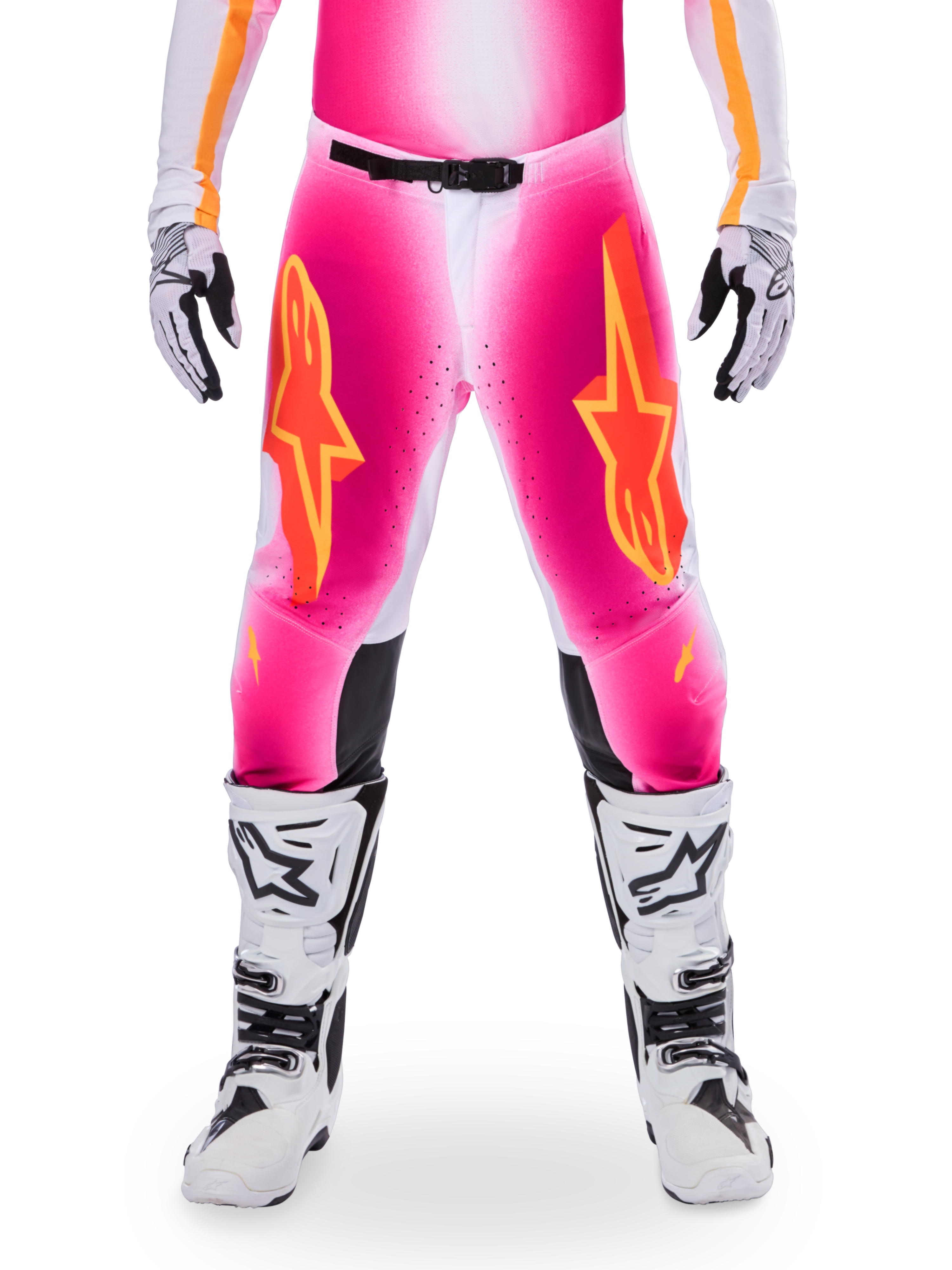 Alpinestars Limited Edition Supertech AFD MIG-byxor, motocross-racingbyxor, fluorescerande rosa och vita med orange detaljer, stora stjärnlogotyper på låren, perforerade paneler och svarta greppzoner vid knäna, bärs med vita och svarta motocross-stövlar