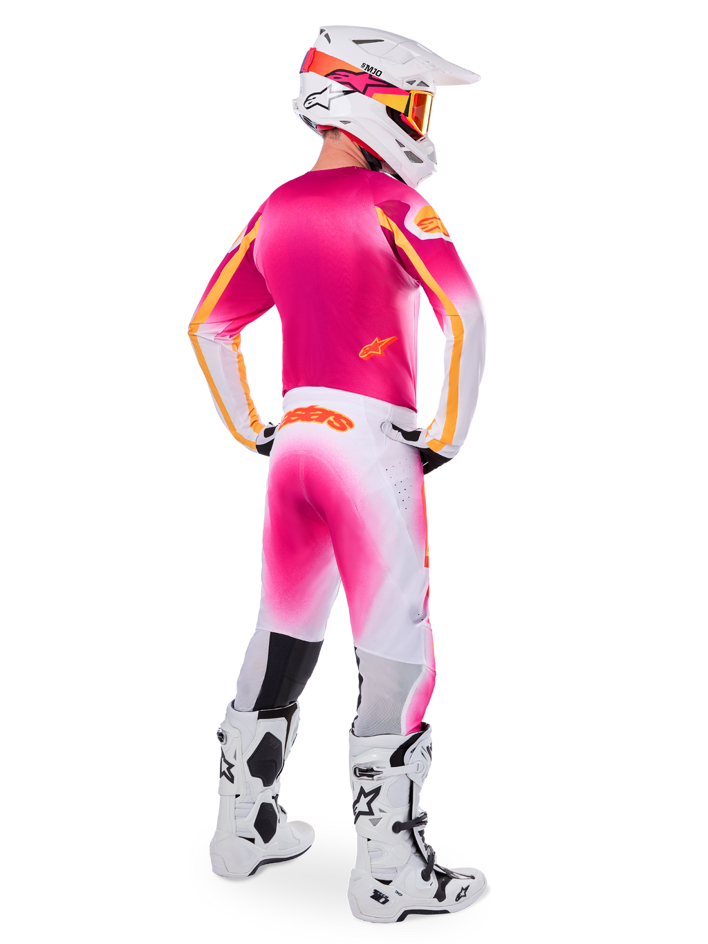 Motocrossförare sedd bakifrån bärande Limited Edition Supertech AFD MIG-utrustningsset, rosa tröja med orangea detaljer, vita byxor med rosa färgövergång och orange Alpinestars-branding, vit hjälm med rosa grafik och orangea goggles, vita och svarta stövlar, professionellt racingställ för terrängkörning