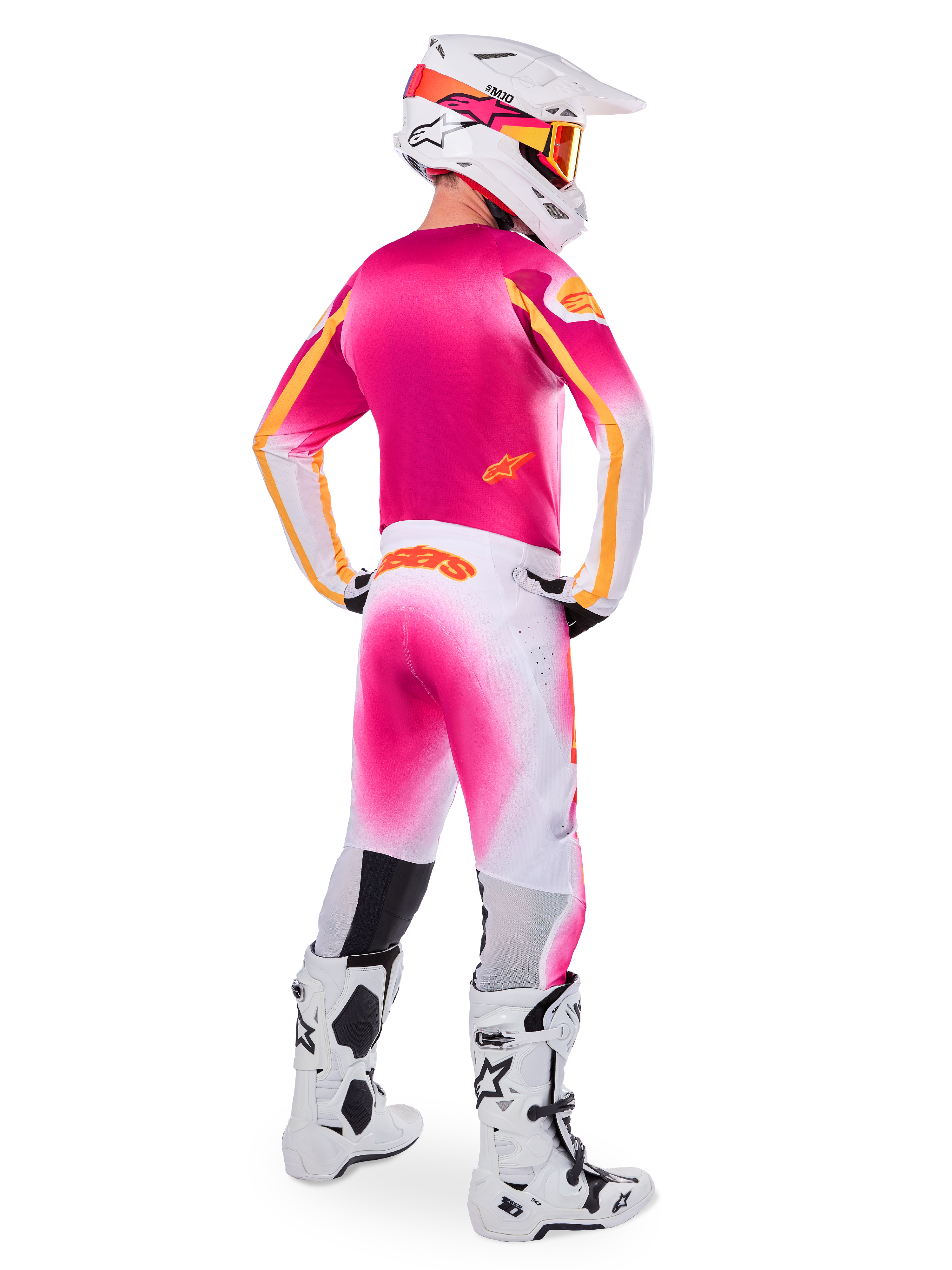 Motocrossförare sedd bakifrån bärande Limited Edition Supertech AFD MIG-utrustningsset, rosa tröja med orangea detaljer, vita byxor med rosa färgövergång och orange Alpinestars-branding, vit hjälm med rosa grafik och orangea goggles, vita och svarta stövlar, professionellt racingställ för terrängkörning