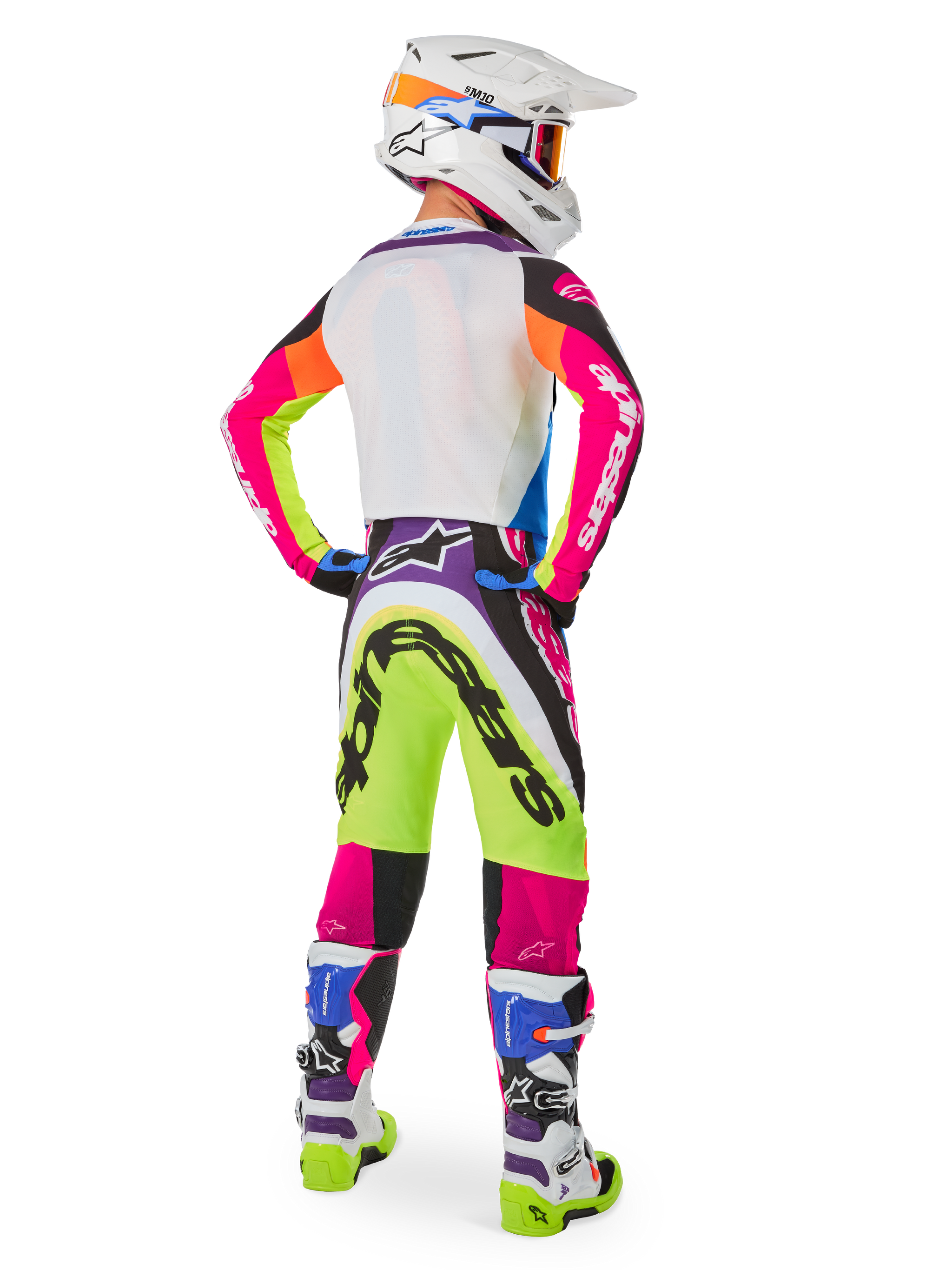Motocross rider from behind wearing Alpinestars Limited Edition Supertech Hay gear, vibrant multicolor Supertech Hay Pants with neon yellow, hot pink, and purple graphics, matching jersey, white helmet, and coordinated white and blue boots, complete off-road racing outfit