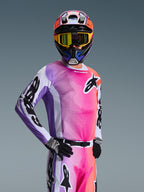 Motocrossförare iförd Alpinestars 2026 Racer Air Portl tröja, multifärgad gradient i rosa, lila och orange med vita detaljer, matchande färgglad hjälm och gula goggles, svarta handskar, professionell utrustning för terrängkörning