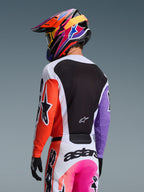 Alpinestars 2026 Racer Air Portl-tröja i Multicolor, motocrossförare sedd bakifrån, orange högerärm, lila vänsterärm, stor svart meshpanel på ryggen för ventilation, matchande byxor och färgstark hjälm, professionell utrustning för terrängkörning.