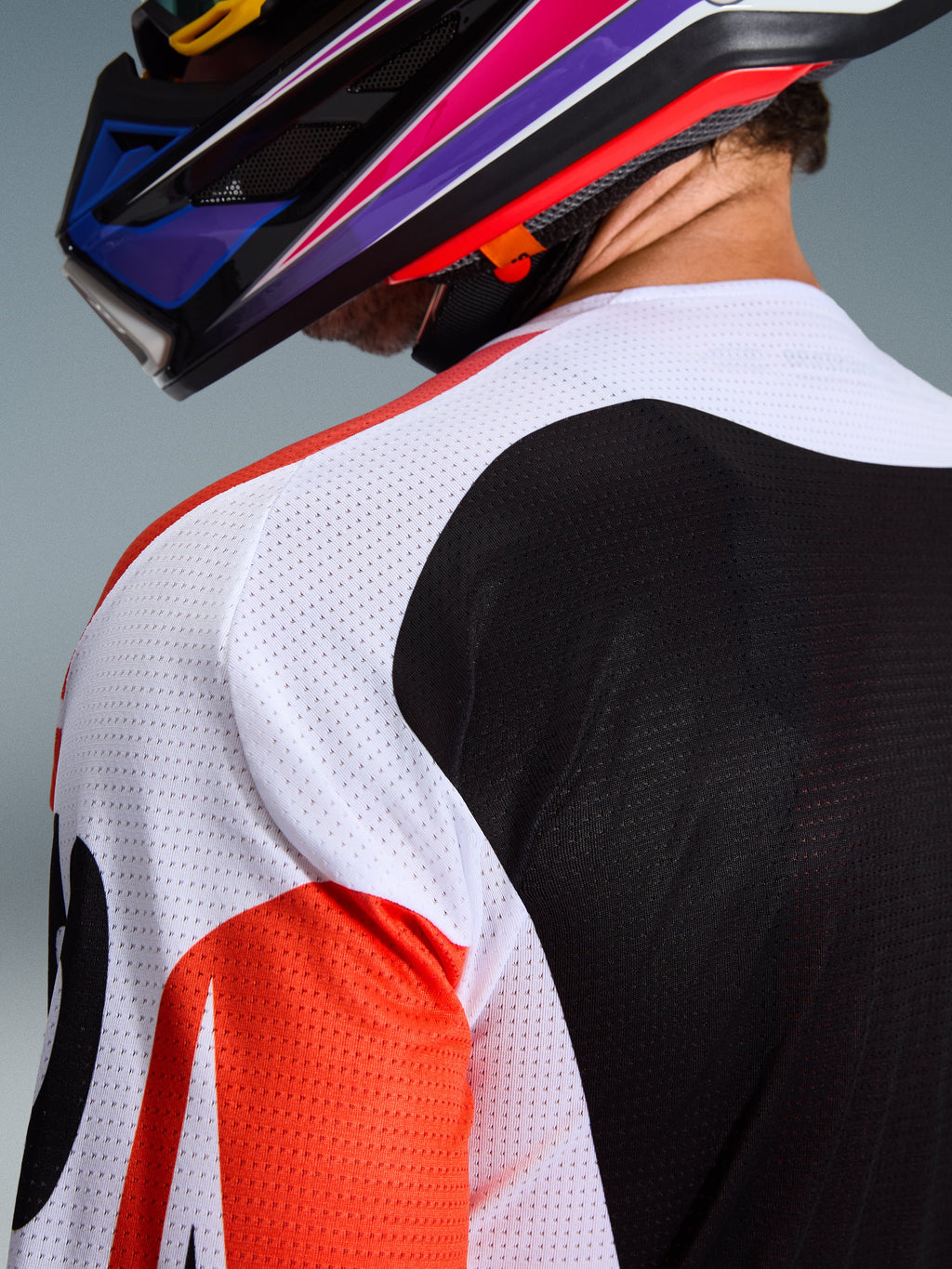 Alpinestars 2026 Racer Air Portl-tröja, motocrosströja, flerfärgad med vita, svarta och röda paneler, närbild på den perforerade mesh-konstruktionen på axeln och ryggen för ventilation, bärs med en färgstark motocrosshjälm