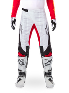 Alpinestars Limited Edition Techstar Deep-byxor, motocrossbyxor, vita med svarta och röda detaljer, stjärnlogotyp och laserperforeringar, visas med vita motocross-stövlar och handskar, hållbart tekniskt material för terrängkörning