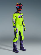Alpinestars 2026 Supertech Vista Pants, Motocross Pants, Neon Yellow and Purple, worn with matching racing jersey, purple boots, and colorful helmet, featuring black leather knee panels, bold purple Astar logos, and perforated ventilation zones, coordinated outfit for off-road racing.