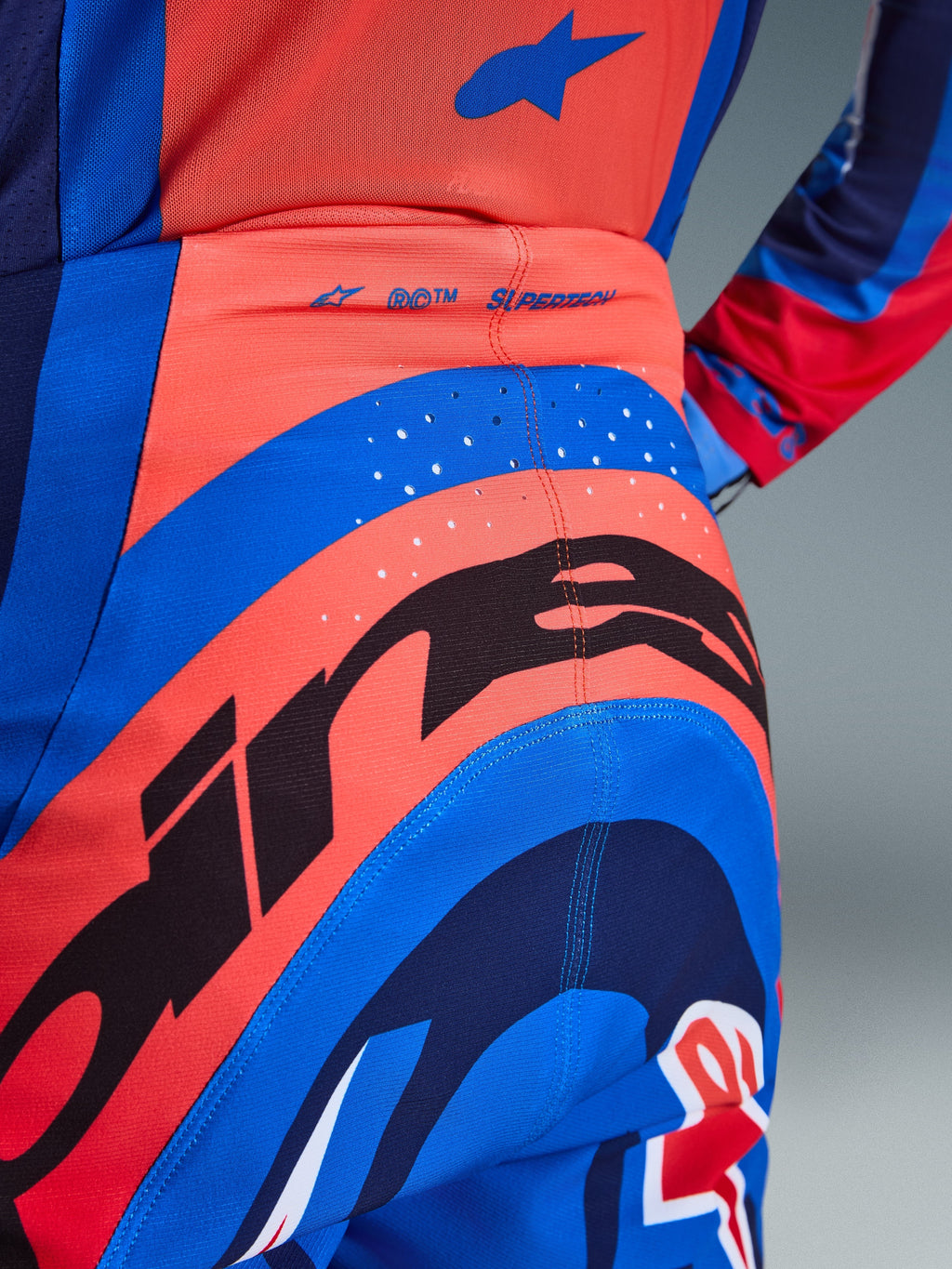 Alpinestars 2026 Supertech Vista byxor, motocrossbyxor, mörkblå, Hot Coral och koboltblå, närbild bakifrån som visar tydlig logotyp, laserskurna perforeringar för ventilation och SUPERTECH-logotyp på midjebandet, performance-stretchmaterial för terrängkörning