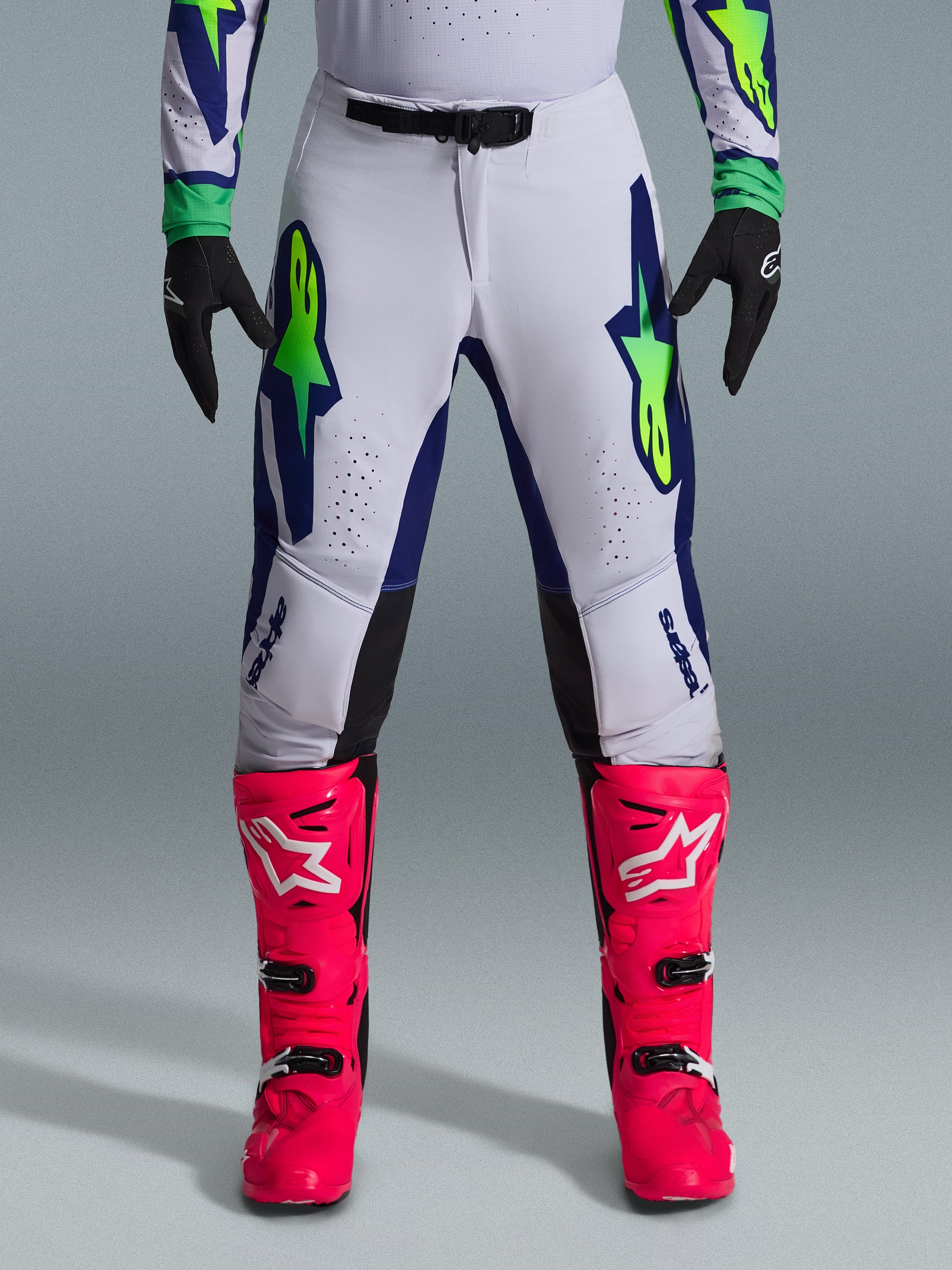 Alpinestars 2026 Supertech Vista-utrustningsset, motocrossbyxor i vitt med blå och limegröna detaljer, matchade med starka rosa stövlar och svarta handskar, racingutrustning av professionell kvalitet med atletisk passform och laserskurna perforeringar.