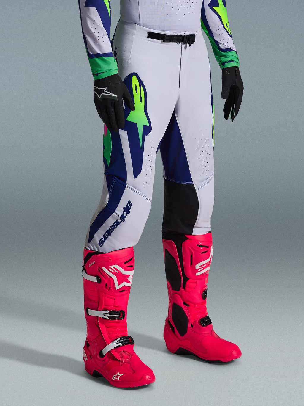 Alpinestars 2026 Supertech Vista byxor, motocrossbyxor, ljusgrå med neongula och blå detaljer, bärs med färgstarka rosa motocross-stövlar och svarta handskar, atletisk racingpassform med hållbar stretchkonstruktion för elitprestanda i terräng