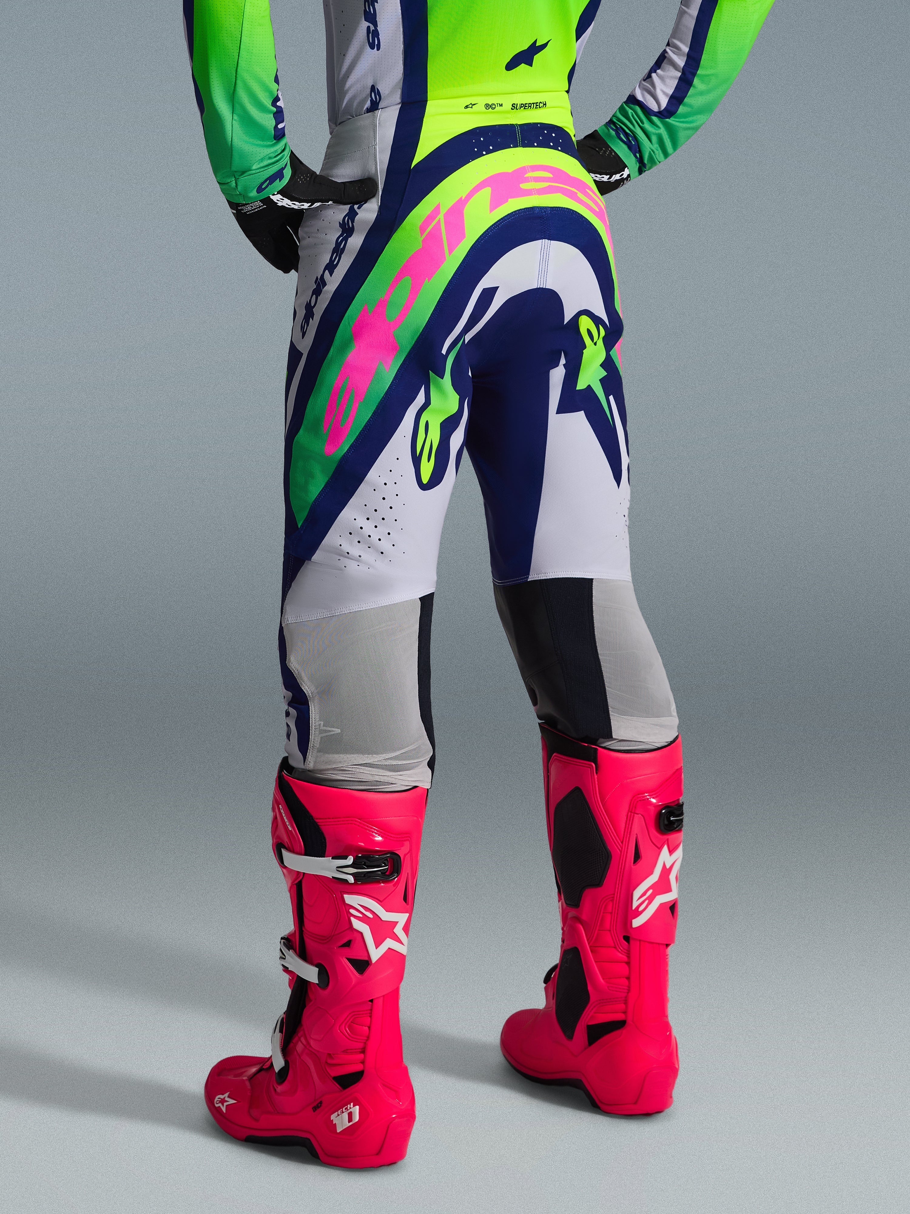 Alpinestars 2026 Supertech Vista Gear Set, bakvy av motocrossutrustning, vita byxor med blå och limegröna paneler, stor rosa logotyp på sätet, kombinerat med livfullt rosa Tech 10-stövlar, professionell racingutrustning för terrängkörning