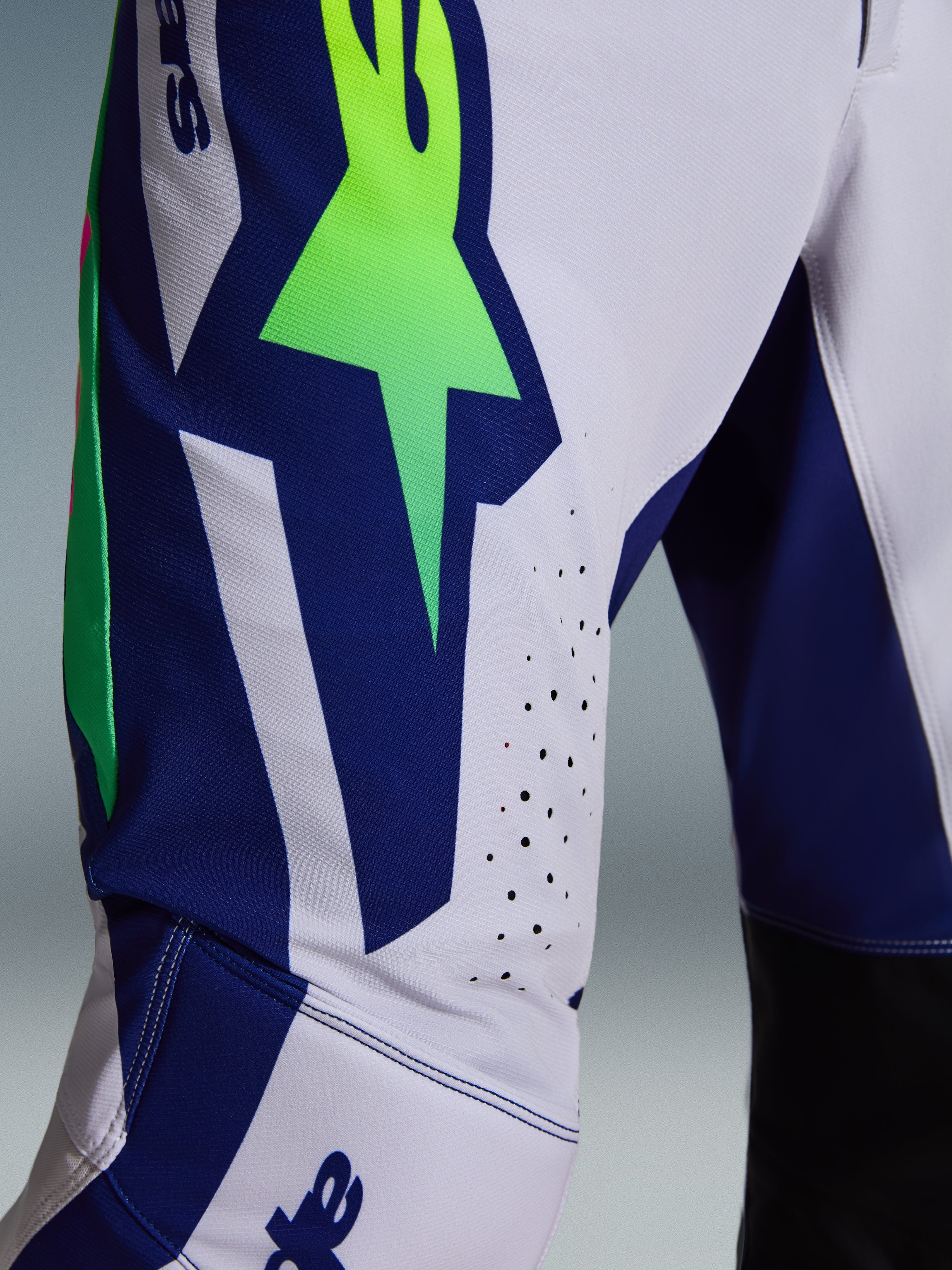 Alpinestars 2026 Supertech Vista byxor, motocrossbyxor, ljusgrå med gul fluo och blå detaljer, närbild på låret som visar den stora A-stjärnlogotypen, laserskurna ventilationshål och avancerat stretch-ripstopmaterial.