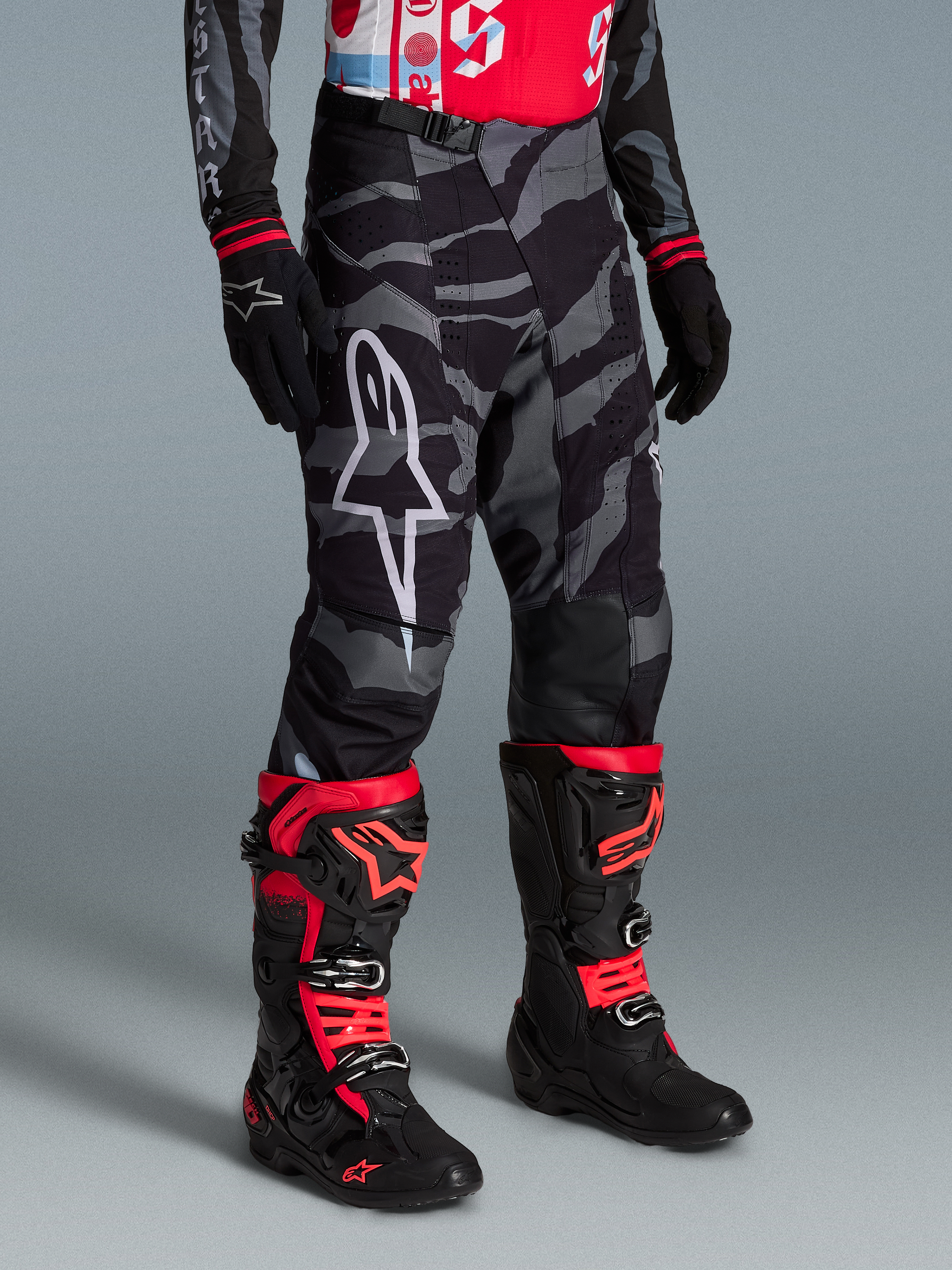Alpinestars Techstar Beast Coast byxor i gråsvart kamouflagemönster med vit logotyp, matchat med röda och svarta racingstövlar.