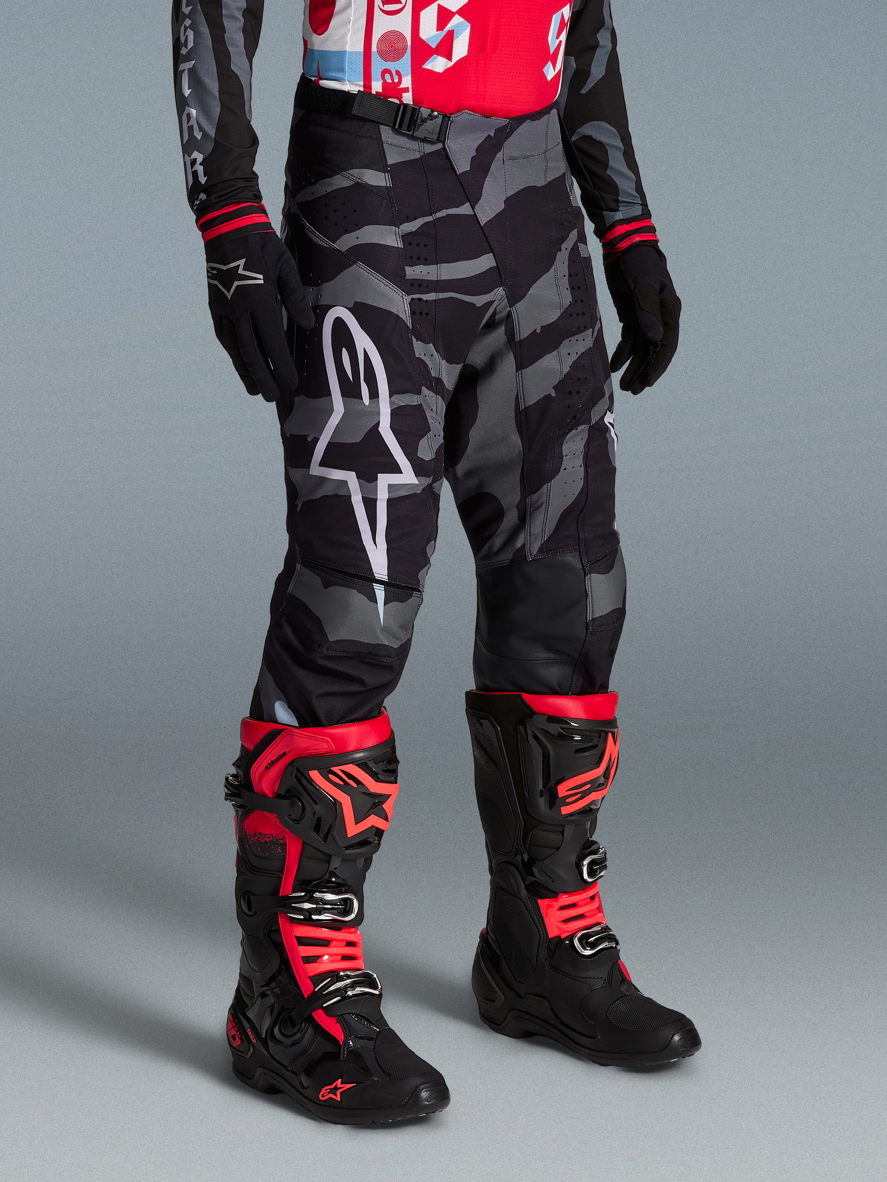 Alpinestars Techstar Beast Coast byxor i gråsvart kamouflagemönster med vit logotyp, matchat med röda och svarta racingstövlar.