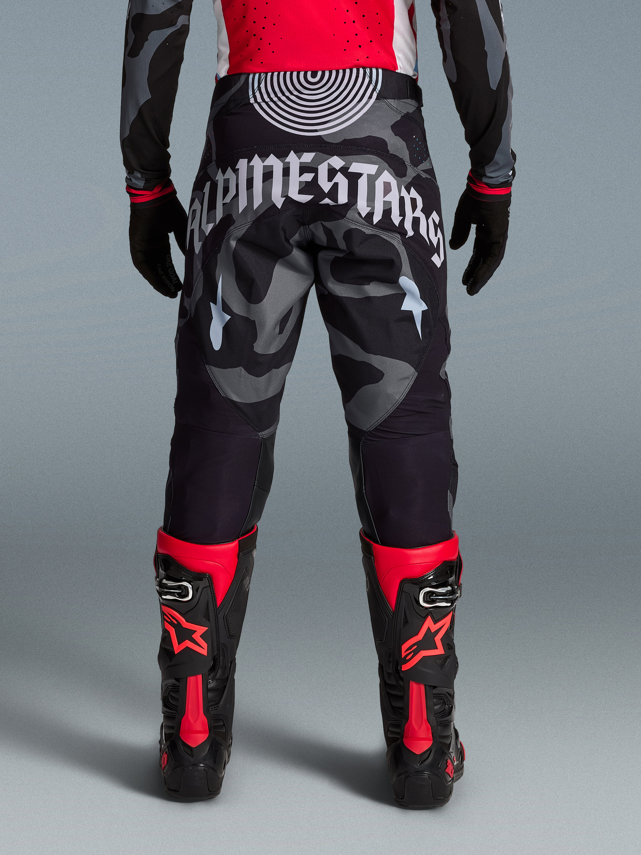Alpinestars Techstar Beast Coast Byxor i gråsvart kamouflage, sedda bakifrån med vit logotyp och röda racingstövlar.