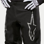 Alpinestars 2024 Fluid Graphite Pants, Motocross Pants, Black and Silver, detail shot of the upper thighs and waist, featuring a large silver star logo on the leg, worn with black and white racing gloves