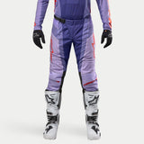 Alpinestars 2024 Techstar Ocuri Pants, motocrossbyxor i lila och marinblått med orange och röda detaljer, röda logotypkonturer på låren, vita stövlar och svarta handskar, ventilationsperforeringar och magnetiskt spänne i midjan, racingdesign för terrängkörning.