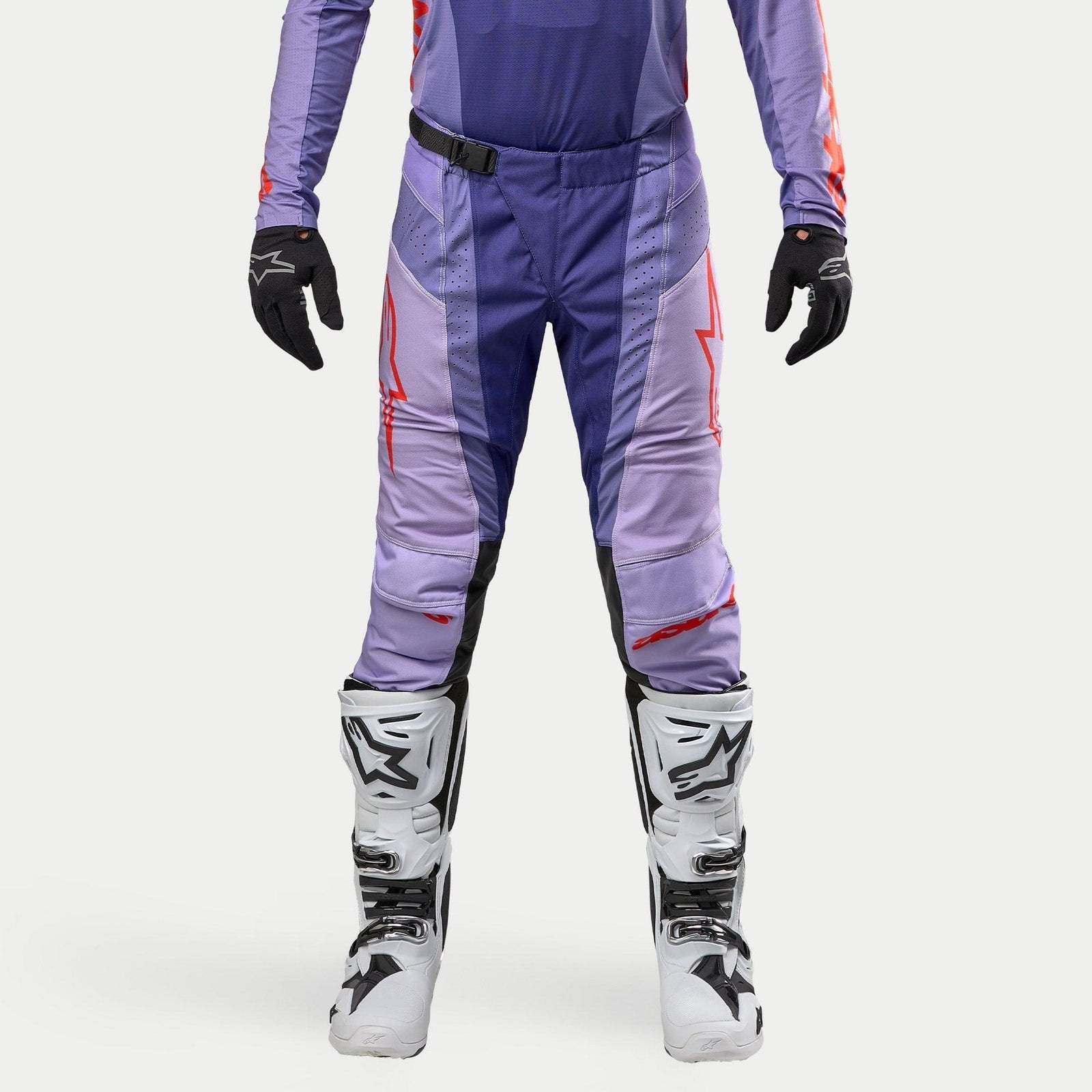 Alpinestars 2024 Techstar Ocuri Pants, motocrossbyxor i lila och marinblått med orange och röda detaljer, röda logotypkonturer på låren, vita stövlar och svarta handskar, ventilationsperforeringar och magnetiskt spänne i midjan, racingdesign för terrängkörning.
