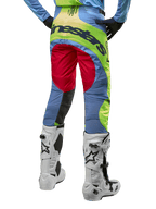 Alpinestars 2024 Techstar Ocuri-byxor, motocrossbyxor, ljusblå, neongula och bärröda, vy bakifrån bärs med vita och svarta motocross-stövlar, med livfull color-blocking och tydlig Alpinestars-logotyp på sätet.