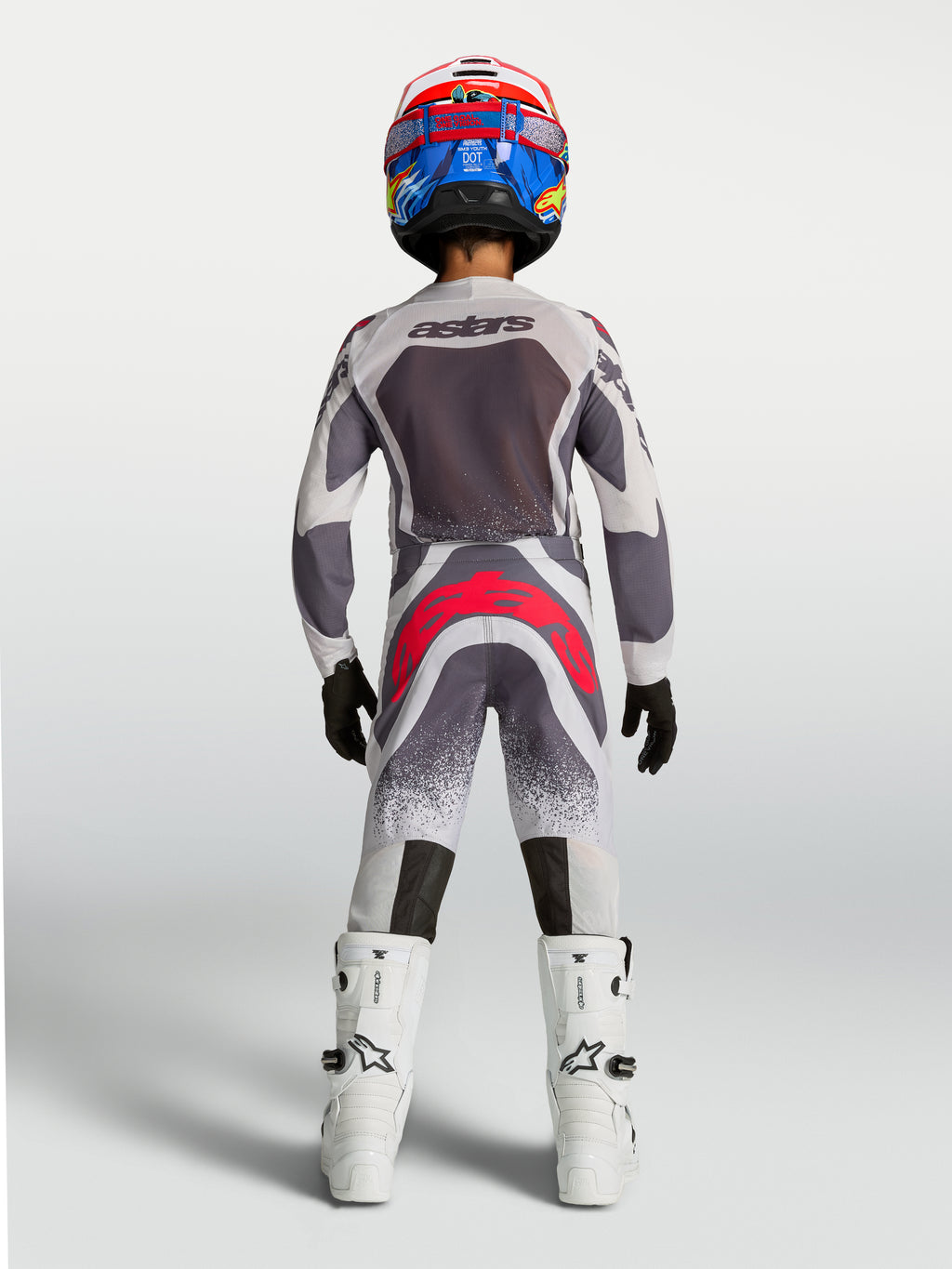 Alpinestars 2027 Supertech Swan ungdomsbyxor, grå och röda motocrossbyxor sedda bakifrån på förare i racingutrustning.