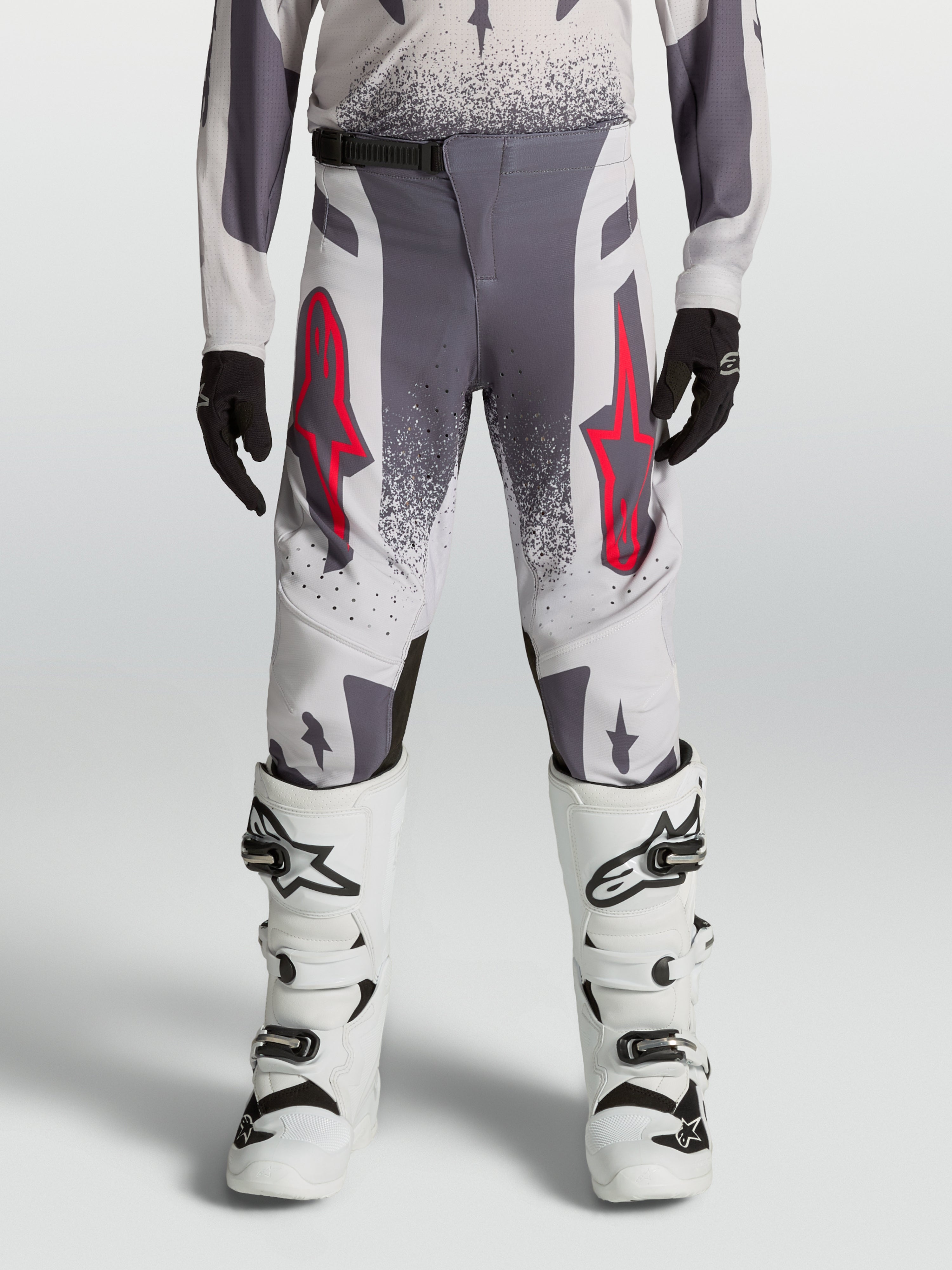 Alpinestars 2027 Supertech Swan ungdomsbyxor, motocrossbyxor för tävling, gråa och lila med röda detaljer, atletisk passform i stretch-ripstop, bärs med vita stövlar för terrängkörning.