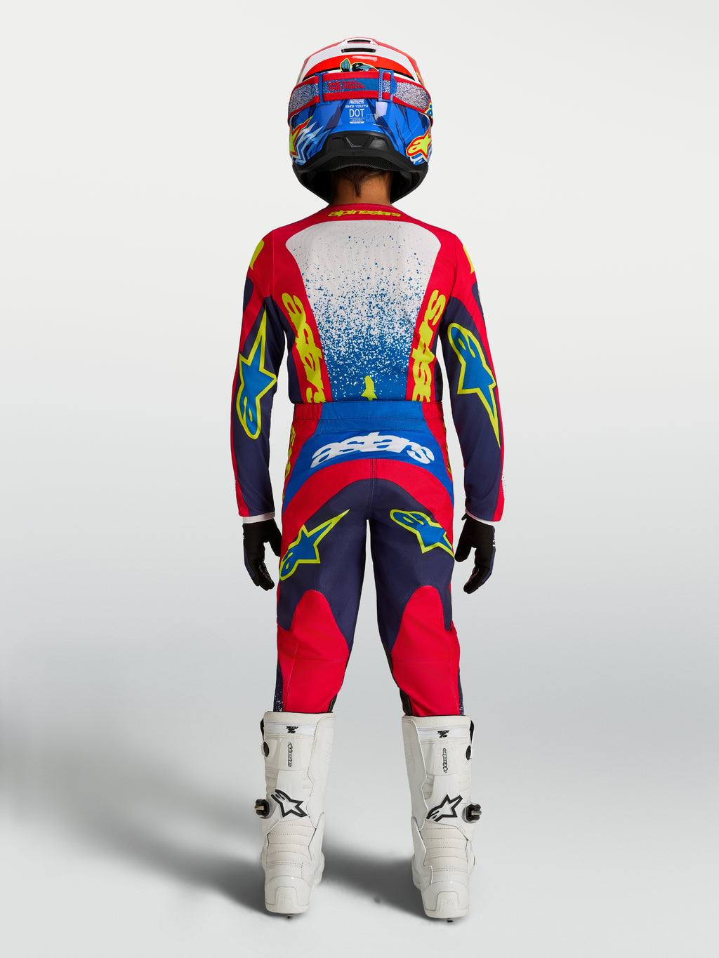 Alpinestars ungdom Fluid Drag byxor och tröja, rött och blått motocrosset med vita stövlar, vy bakifrån.