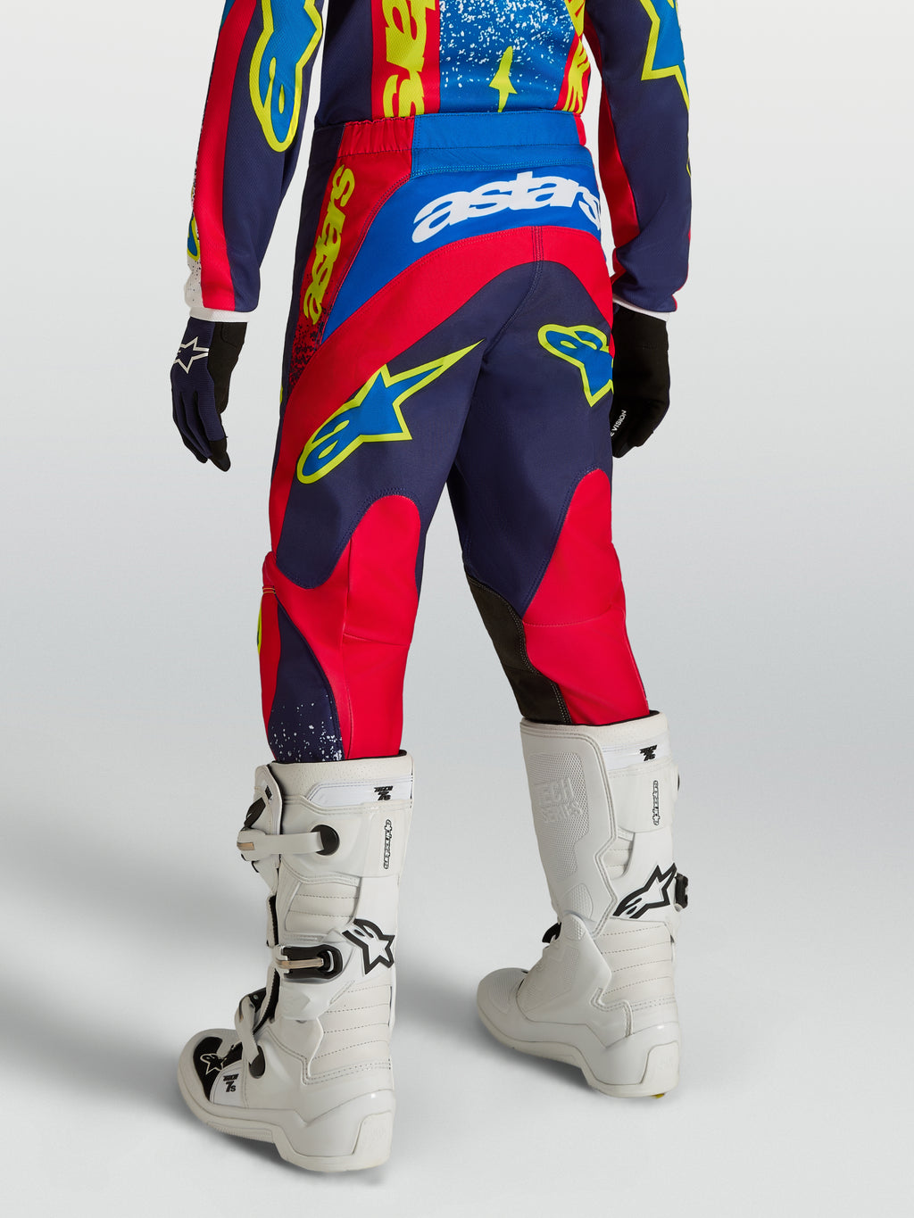 Alpinestars 2027 Ungdom Fluid Drag byxor, marinblå och röda motocrossbyxor, vy bakifrån med vita stövlar.