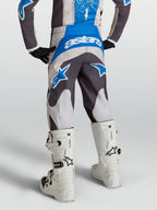 Alpinestars Fluid Drag motocrossbyxor för ungdom, grå och blå, sedda bakifrån på en förare med vita stövlar.