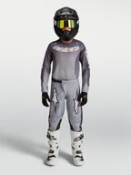 Alpinestars 2027 Fluid Amber ungdomsbyxor, grå och sandfärgade motocrossbyxor i 600D-polytyg, visas med matchande utrustning.