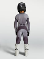Alpinestars 2027 Fluid Amber ungdomsbyxor, motocrossbyxor för terrängkörning, sandfärgade och gråa, vy bakifrån på en förare, slitstarkt 600D-polytyg med stretchpaneler.