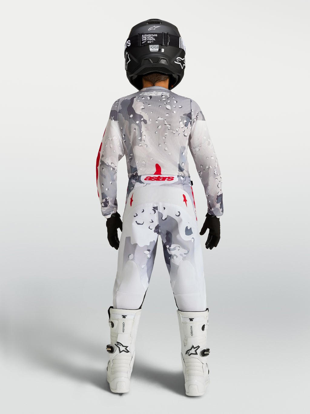 Alpinestars 2027 Ungdom Fluid Lone byxor, motocrossbyxor för barn, gråa och vita med kamouflagemönster, ryggvy på modell med full utrustning, slitstark design för terrängkörning.