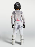Alpinestars 2027 Ungdom Fluid Lone byxor, motocrossbyxor för barn, gråa och vita med kamouflagemönster, ryggvy på modell med full utrustning, slitstark design för terrängkörning.