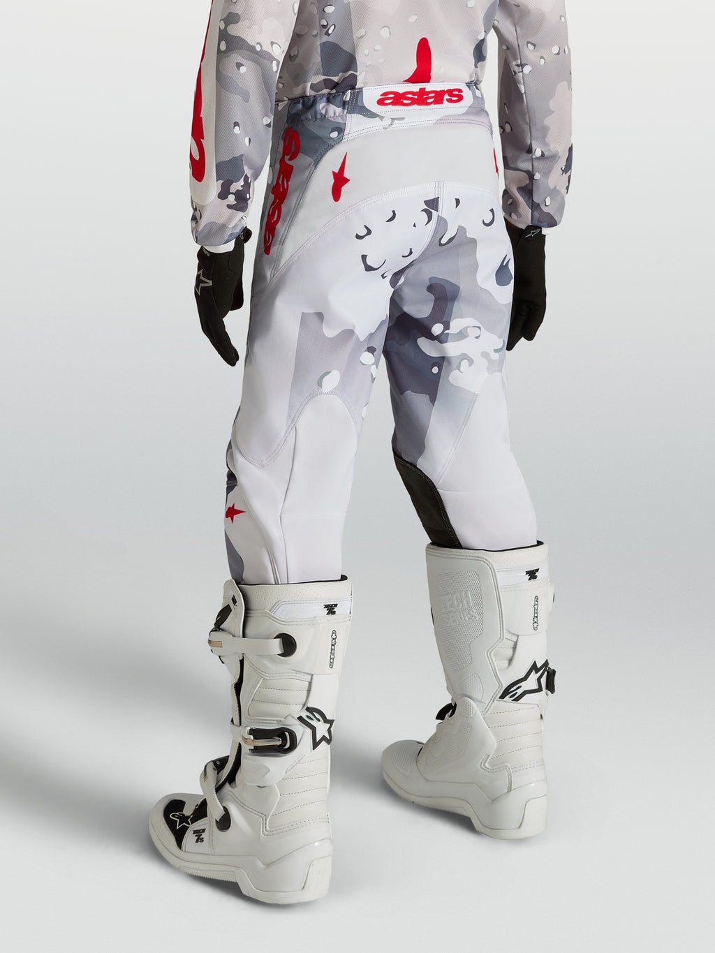 Alpinestars Ungdom Fluid Lone byxor, grå kamouflage och röda motocrossbyxor, sedda bakifrån med vita stövlar.