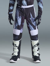 Alpinestars 2026 Youth Fluid Lahnd-byxor, motocrossbyxor för ungdom, Iron Camo med vita detaljer, bärs med svartvita offroad-stövlar och handskar, slitstark design för unga förare.