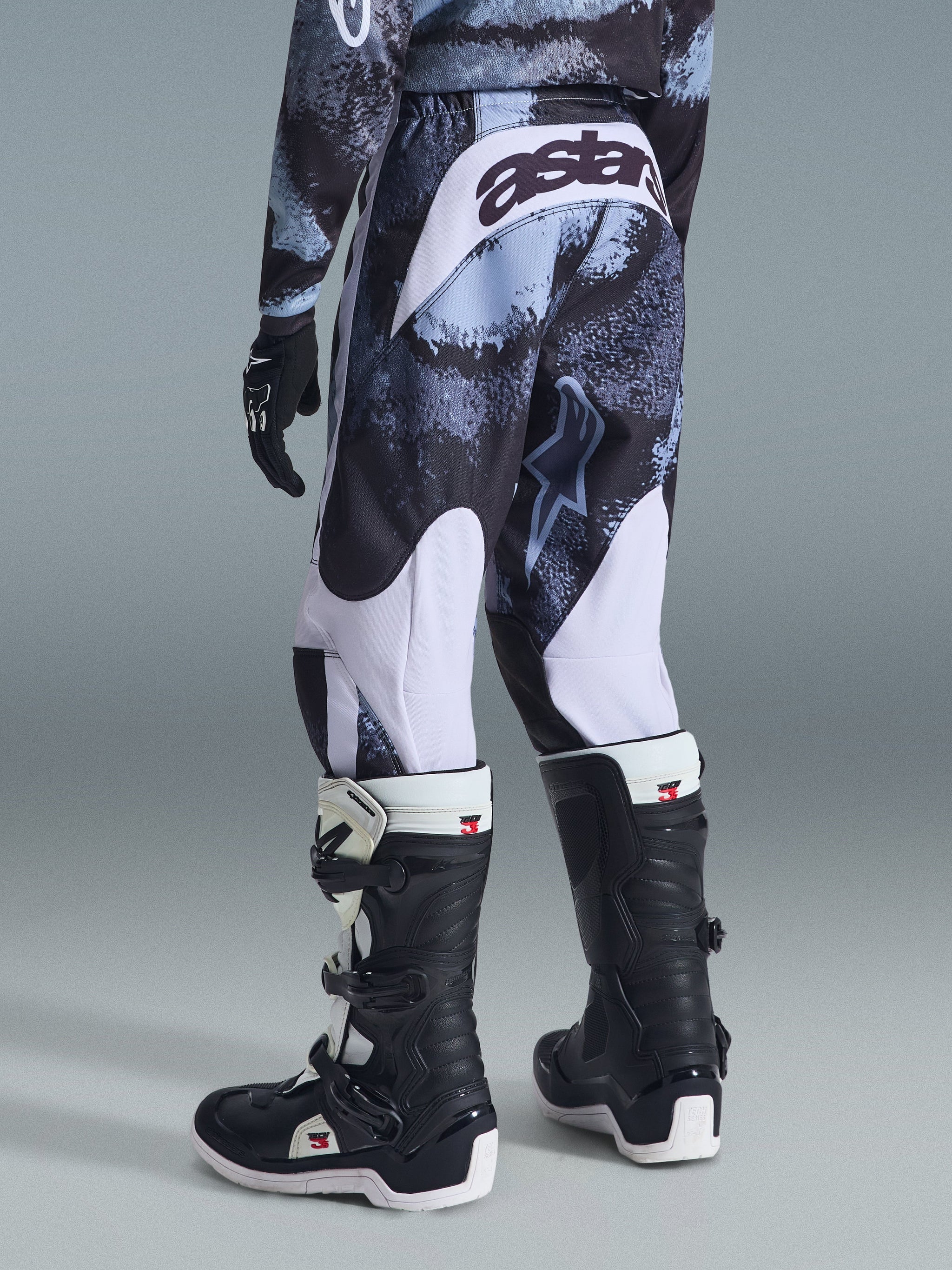 Alpinestars 2026 Youth Fluid Lahnd-byxor, motocrossbyxor, Iron Camo med vita detaljer, vy bakifrån som visar ”astars”-logotyp på sätet, bärs med matchande camotröja och svartvita Tech 3-motocross-stövlar.