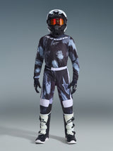 Alpinestars 2026 Fluid Lahnd byxor för ungdom, motocrossbyxor, Iron Camo, bärs av en ung förare med matchande camotröja, svart hjälm med orangea goggles och vita och svarta stövlar, med en koordinerad design med tydliga logotyper och förstärkta paneler för terrängkörning