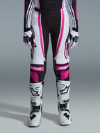 Alpinestars 2026 Stella Techstar Nomur byxor för dam, motocrossbyxor, svart, vit och fuchsia, bärs med matchande racingtröja, handskar och vita motocross-stövlar, med framträdande rosa grafik och astars-logotyper på knäna, designade för terrängtävling på hög nivå.