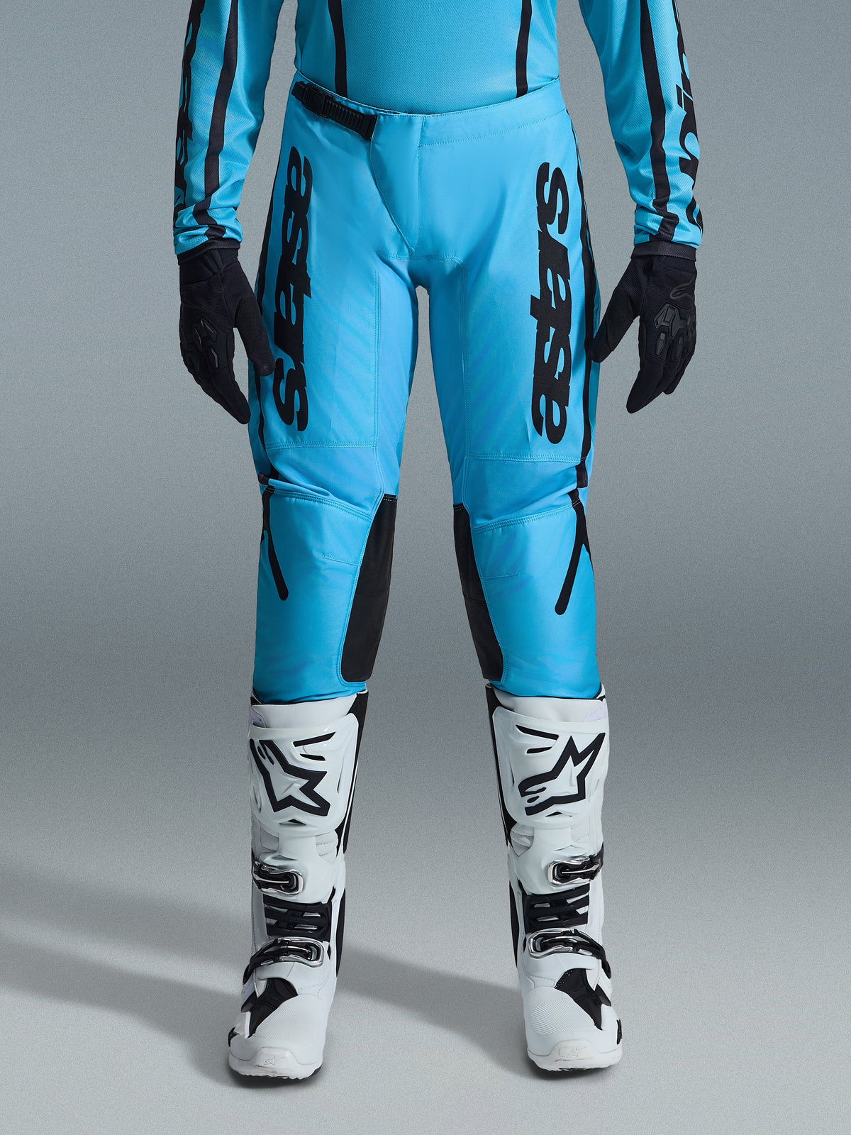 Alpinestars 2026 Stella Fluid Apex-byxor för dam, motocrossbyxor, klar cyan och svart, vertikal svart logotyp på låren, svarta förstärkta paneler på knänas insida, visas med vita och svarta motocross-stövlar och svarta handskar, professionell offroad-utrustning för damer
