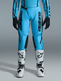 Alpinestars 2026 Stella Fluid Apex-byxor för dam, motocrossbyxor, klar cyan och svart, vertikal svart logotyp på låren, svarta förstärkta paneler på knänas insida, visas med vita och svarta motocross-stövlar och svarta handskar, professionell offroad-utrustning för damer